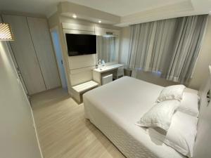 1 dormitorio con 1 cama blanca y TV en Hotel Marimar The Place, en Balneário Camboriú