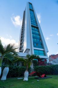 un edificio alto con palmeras delante en Roomo Praia de Boa Viagem Residencial, en Recife