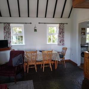 a dining room with a table and chairs and two windows at Traditional Cosy Cottage in Louisburgh