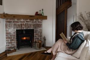 una mujer sentada en un sofá leyendo un libro en Gatekeepers Lodge - A Historic Hobart Experience en Hobart