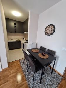 a dining room table with chairs and a clock on a wall at Apartman Bedem in Čačak
