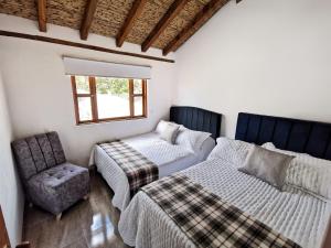 ein Schlafzimmer mit zwei Betten, einem Stuhl und einem Fenster in der Unterkunft Cabaña San Miguel Arcangel in Villa de Leyva