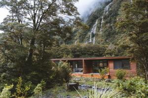 a cabin in the mountains with a waterfall in the background at Milford Sound Lodge in Milford Sound