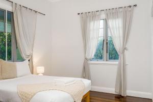 a white bedroom with a bed and two windows at Skye Lodge - 7 Bedroom charming Balinese retreat with designer pool in Byron Bay +4 photos