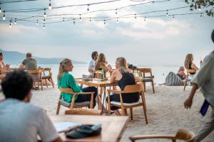 grupa ludzi siedzących przy stolikach na plaży w obiekcie Mowies Gili Air w Gili Air