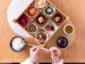 a person holding chopsticks in front of a tray of food at Mitsui Garden Hotel Ginza-gochome in Tokyo