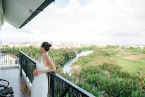 a woman in a white dress standing on a balcony overlooking a river at Shining Riverside Hoi An Boutique & Spa in Hoi An