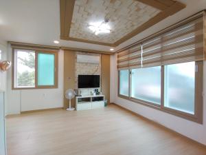 a living room with a flat screen tv and windows at Jeju Oreum Pension in Jeju