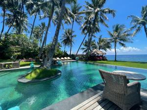 a pool at a resort with palm trees and the ocean at Louka Beach Bali in Tianyar