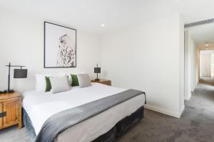 a white bedroom with a large white bed with green pillows at Boutique Stays - Victoria Road in Melbourne