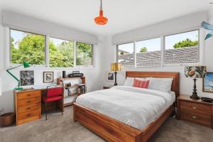 a bedroom with a bed and a desk and windows at Boutique Stays - That 70s House in Mount Waverley