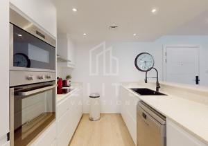 a white kitchen with a sink and a clock on the wall at Fully Furnished 1BR Apartment with Stunning Interior in Dubai