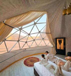 two people sitting on beds in a room with a large window at MARS lUXURY CAMP WADI RUM in Wadi Rum