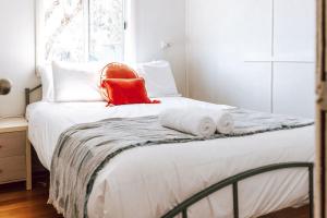 a white bed with an orange pillow on top of it at Bay of Fires - Beachfront - Sloop Cottage in Binalong Bay