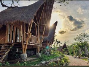 un edificio con techo de paja con el sol en el fondo en Penida Bambu Green en Nusa Penida