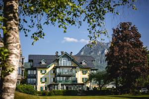 ein großes gelbes Haus mit einem Berg im Hintergrund in der Unterkunft Hotel Brandauers Villen Superior in Strobl