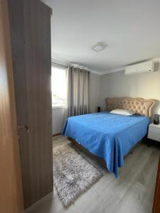 ein Schlafzimmer mit einem Bett mit einer blauen Decke und einem Fenster in der Unterkunft Apto duplex Lagoa do Violão in Torres