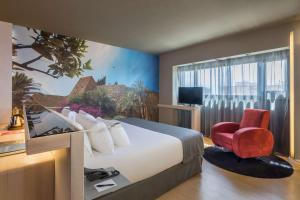 a hotel room with a large bed and a red chair at Barceló Malaga in Málaga