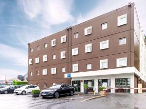 a large brown building with cars parked in a parking lot at ibis Budget Villemomble in Villemomble