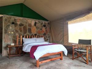 - une chambre avec un lit et un mur en pierre dans l'établissement Resian Mara Camp, à Talek