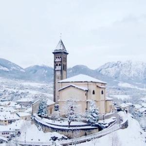 a large building with a clock tower in the snow at Appartamenti Pichler in Castello di Fiemme