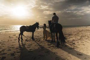 帕傑的住宿－Kinazi Upepo Beach Eco Lodge，一名男子和一名女子在海滩上骑马