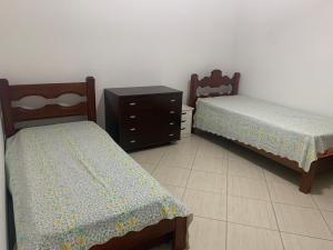 two beds sitting next to a dresser in a room at Apartamento Astúrias a menos de 50m da praia in Guarujá
