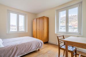 a bedroom with a bed and a desk and two windows at Le Claudel - Idéal pour découvrir les Vosges in La Bresse