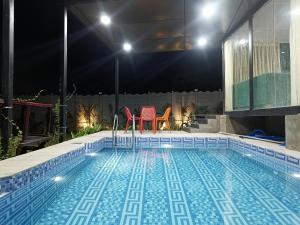 uma piscina à noite com duas cadeiras vermelhas em Bliss Farm Stay- Tulip em Secunderābād