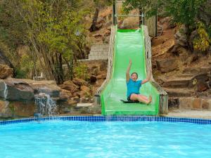 Ein Mann ist auf einer grünen Rutsche in einem Pool in der Unterkunft Waterberg Game Park in Mokopane