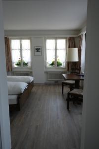 a bedroom with a bed and a desk and windows at Gasthof Löwen in Melchnau
