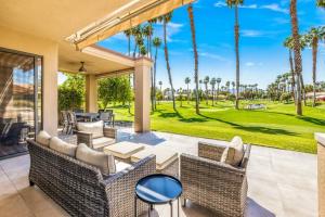 an outdoor patio with wicker furniture and palm trees at Beautiful Condo with Mountain & Sunset Views! in Palm Desert