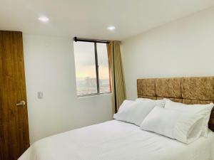 波哥大的住宿－Alquiler Apartamento en Bogotá cerca al aeropuerto-Colibri Dorado，一间卧室配有一张带白色床单的床和一扇窗户。