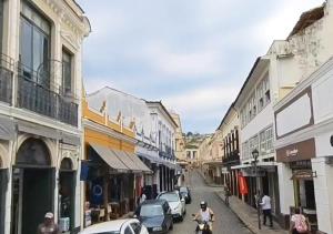 uma rua da cidade com carros e pessoas em uma moto em Flat aconchegante no Centro Histórico em São João del Rei