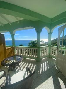 a balcony with chairs and a table and the ocean at Greenhouse on the Hill, Sea View Studio Apartment in Laborie