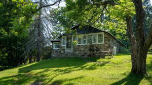 a stone house on a grassy hill with a tree at Cobblestone Cottages in Sharbot Lake