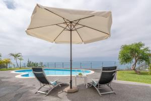 een tafel en stoelen met een parasol naast een zwembad bij Belo Mar in Arco da Calheta