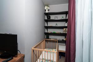 a room with a crib and a shelf with a television at Слънчев Апартамент с Балкон до болница Света София in Sofia