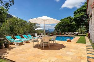 eine Terrasse mit Stühlen und einem Sonnenschirm neben einem Pool in der Unterkunft Casa em Araras: Piscina, sauna e serviço incluído! in Araras Petropolis