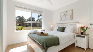 a white bedroom with a bed and a window at Salty Marlin in Callala Bay