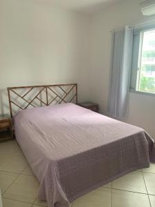 ein Schlafzimmer mit einem Bett mit einer lila Bettdecke und einem Fenster in der Unterkunft Apartamento Astúrias a menos de 50m da praia in Guarujá