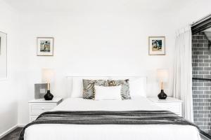 a white bedroom with a white bed and two lamps at 11 James Cook Apartments - w. pool & beach access in Byron Bay +11 photos