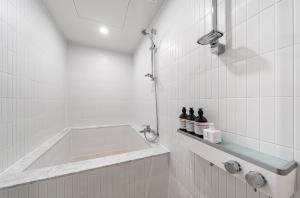 a bath tub in a white tiled bathroom at Browndot Hotel Yeosu Yeocheon in Yeosu
