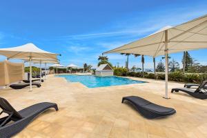 una piscina con sillas y sombrillas en Waterfront Apartment 216, en The Entrance 2 fotos más