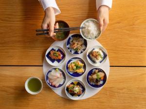 a plate of food on a table with a person holding chopsticks at Mitsui Garden Hotel Fukuoka Gion in Fukuoka