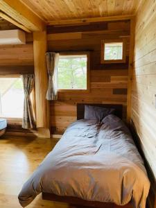 a bed in a log cabin with two windows at 一度だけでも体験してほしいイエローシーダーハンドカットカナディアンログハウス in Karuizawa
