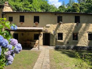 una antigua casa de piedra con un patio con flores púrpuras en Molin Barletta - Nice Holiday House With Private Pool Marliana, Toscana en Marliana