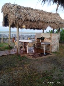 a patio with a table and a grill and a straw hut at Chalé MAAR in Itarema