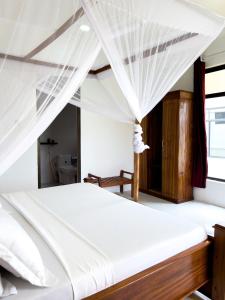 una camera da letto con letto con lenzuola e tende bianche di Kijiji Villas Nungwi a Banda Kuu