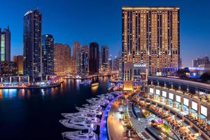 Address Marina Mall Suites "Full Marina Views & Balcony " في دبي: مدينة في الليل فيها قوارب في الماء
